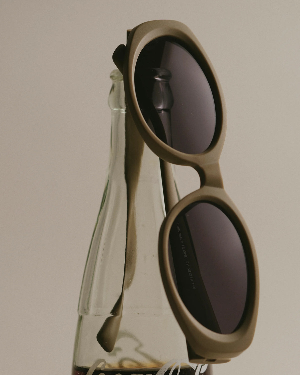 TUDI Leone eyewear, styled still life, khaki frame; dark lenses