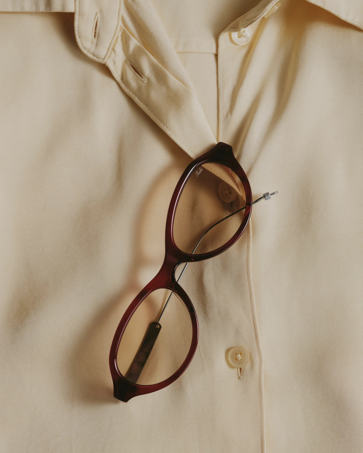 TUDI Riko eyewear, styled still life, wine-red frame; rose-tinted lenses