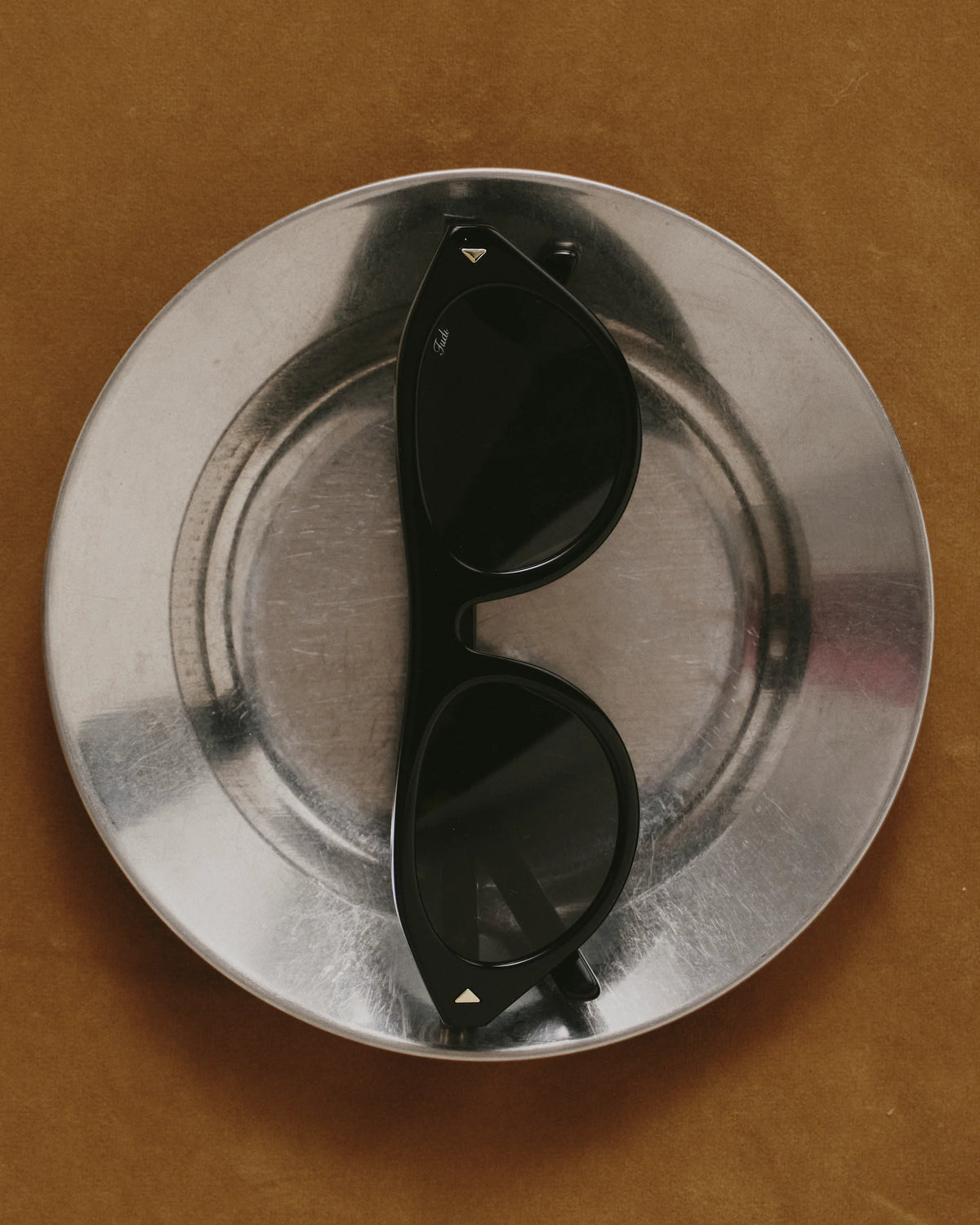TUDI Rocky eyewear, styled still life, black frame; dark lenses